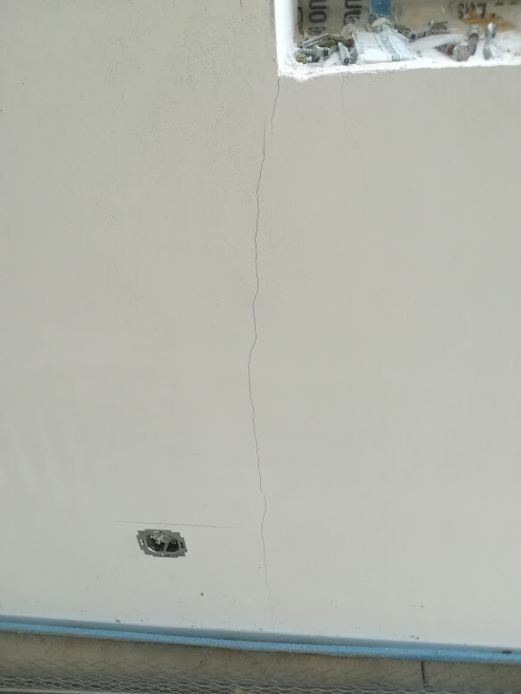 Wand mit senkrechtem Riss, offenes Steckdosenloch unten und Fensteröffnung oben mit Zeitung.