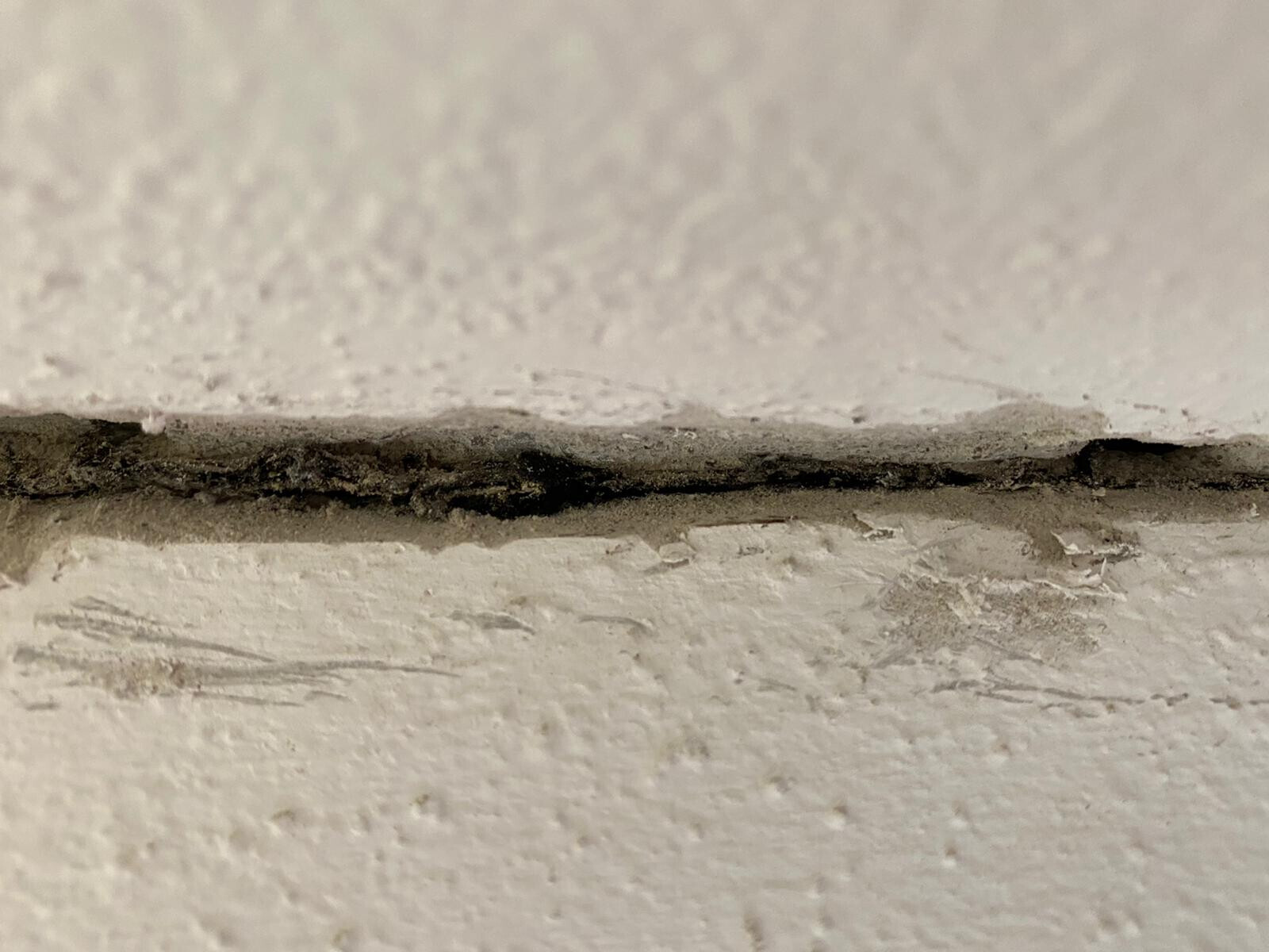 Nahaufnahme eines Risses in einer weißen Wand mit Staub und Ablagerungen.