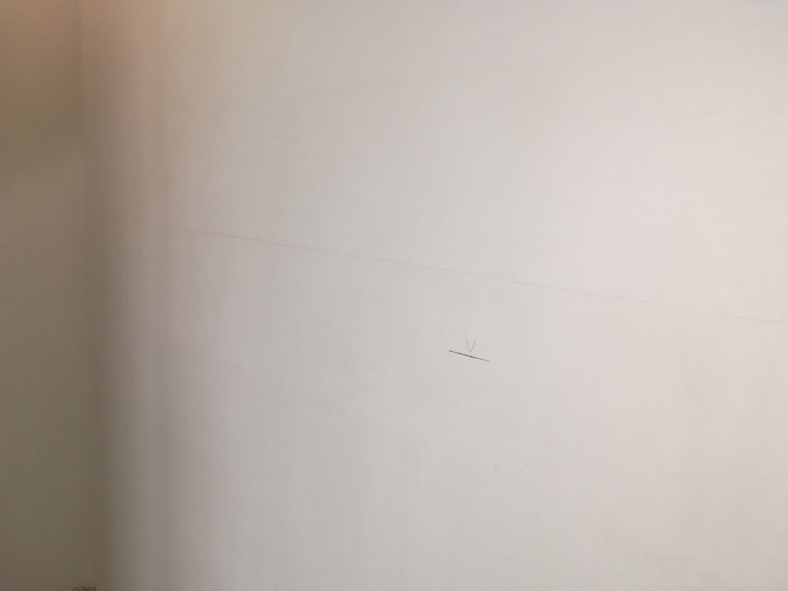 Beigefarbene Wand mit feiner horizontaler Risslinie und kleinem Markierungsstrich.