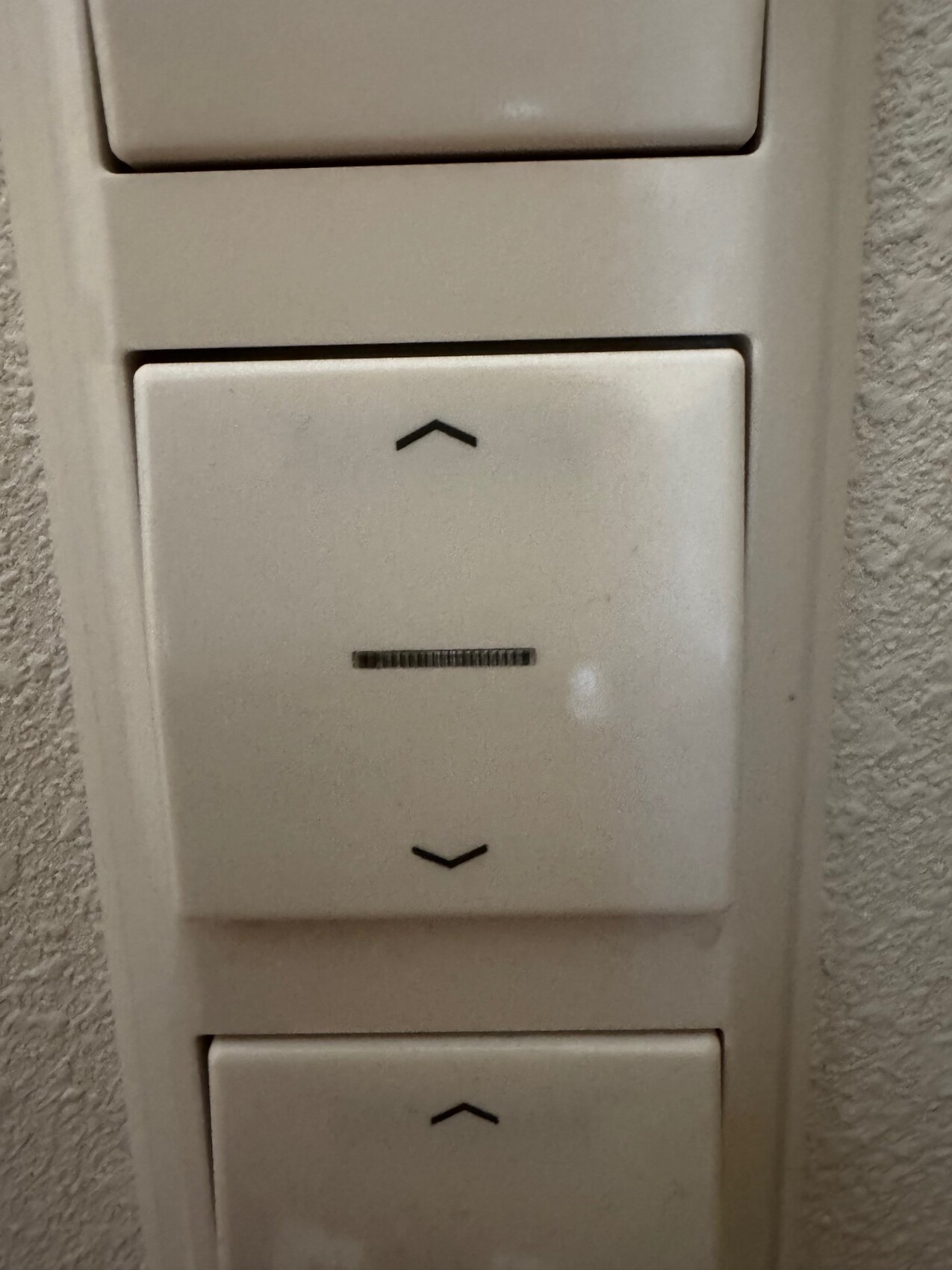 Mittlerer Wandlichtschalter mit Auf- und Ab-Pfeilen und kleinem Reglerstrich; weitere Schalter daneben.