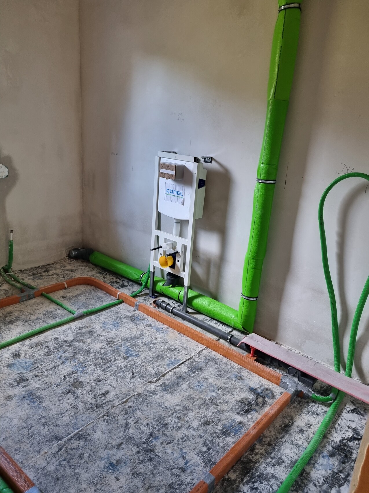 Installationsrahmen für Wand-WC; grüne isolierte Rohre an Wand und Boden.