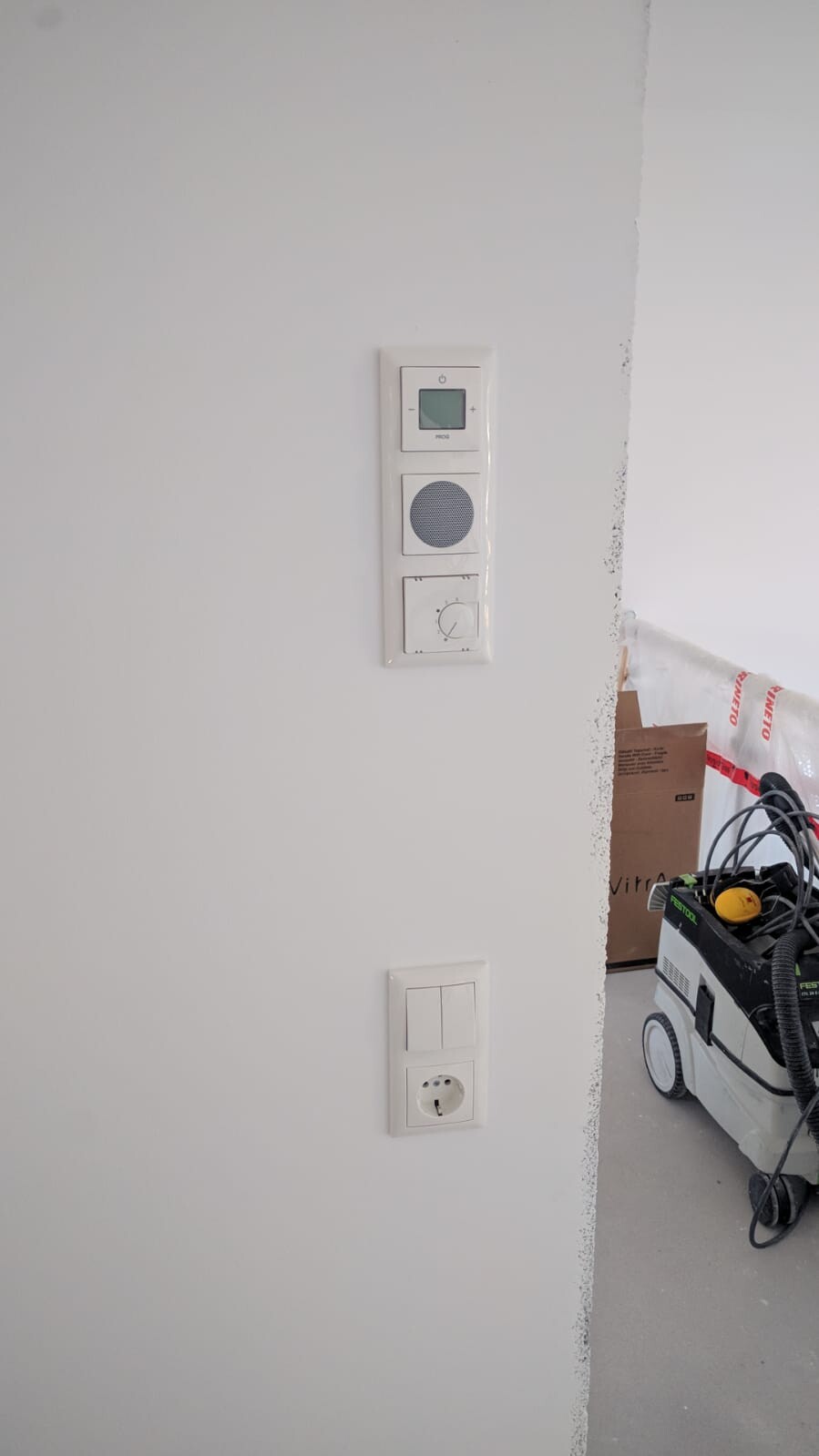Weiße Wand mit Thermostat, Lautsprecher und Steckdose; Bauwerkzeug rechts.