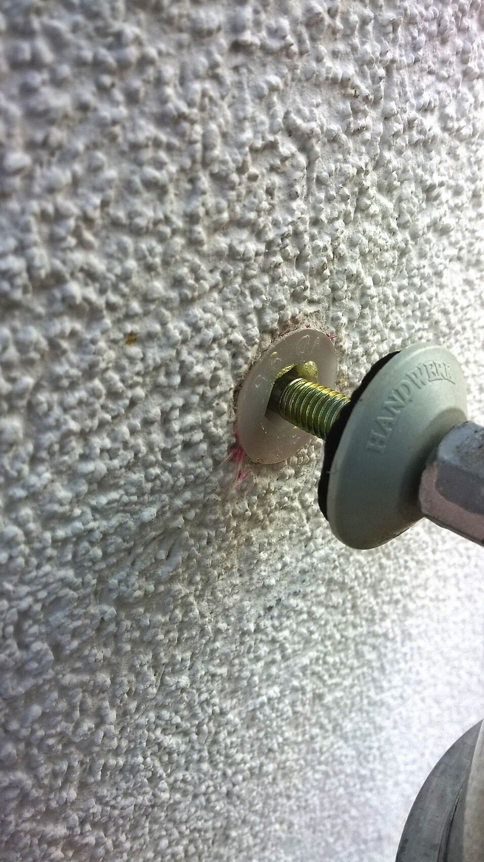 Nahaufnahme eines Wandankers im rauen Putzwand beim Einbau mit Werkzeug