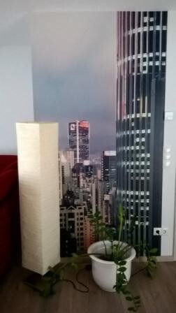 Wohnzimmer mit Wandbild einer städtischen Skyline, Pflanze im weißen Topf und Stehlampe.
