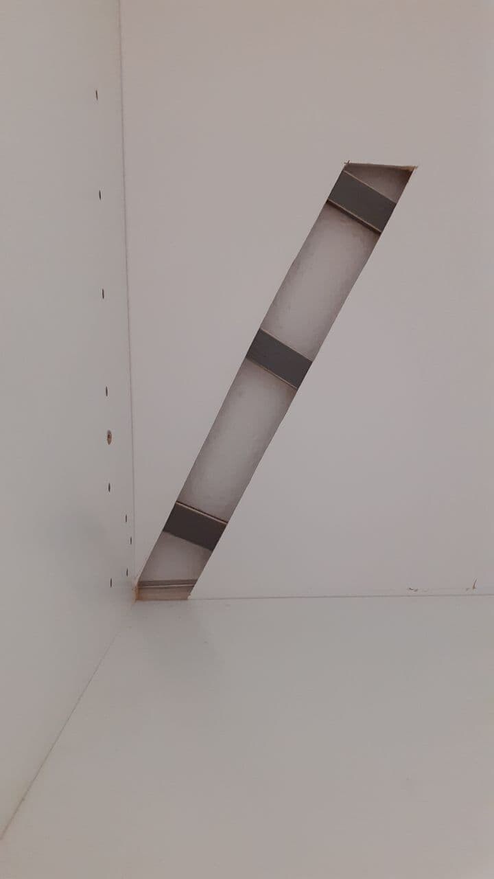 Schräger Schlitz in einer weißen Wand mit Metallstreifen und Innenraum.