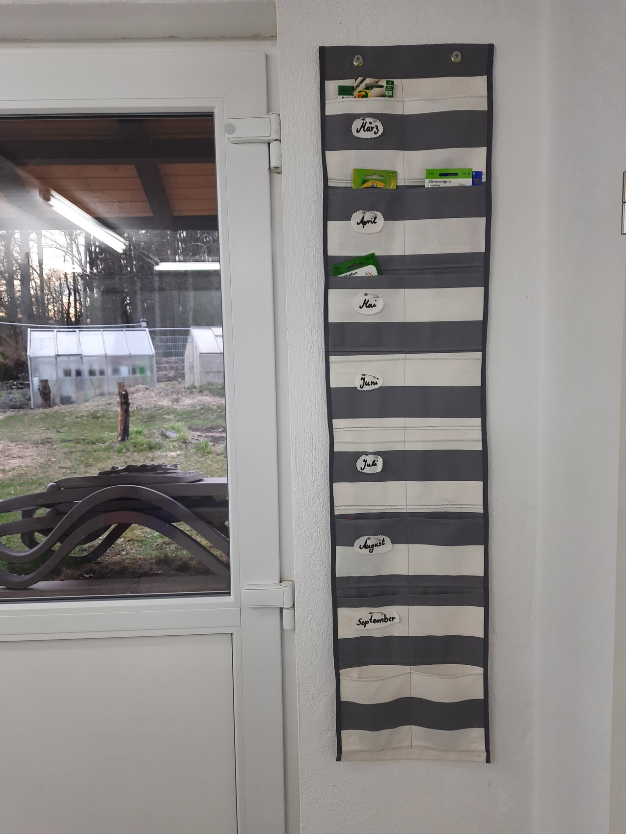 Schlankes, gestreiftes Monats-Organizer mit Fächern März–September an der Wand neben der Tür.