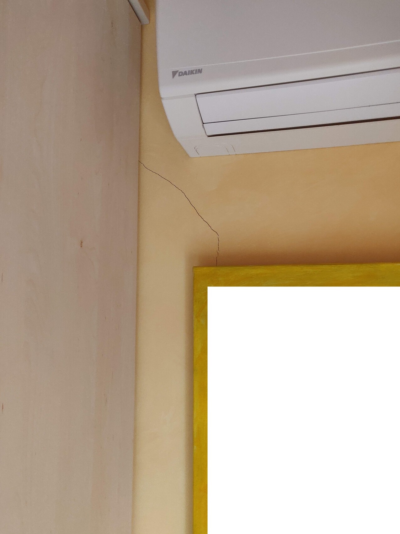 Winkel im Raum mit Daikin-Klimagerät, Wandriss und goldener Bilderrahmen unten rechts.