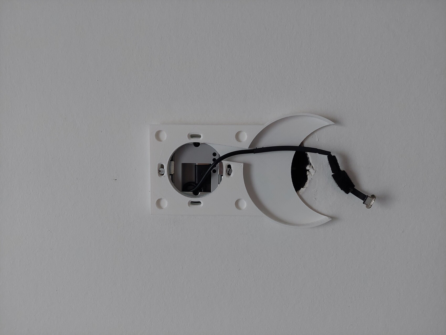 Weißer Wandlampenhalter mit halbmondförmigem Abdeckteil und loses Kabel.