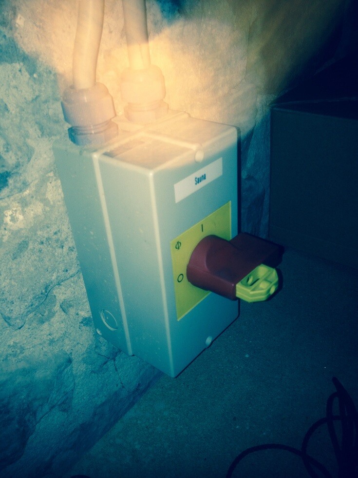 Wandmontierte Haustechnik-Einheit mit grünem Stecker im Keller an rauer Steinwand