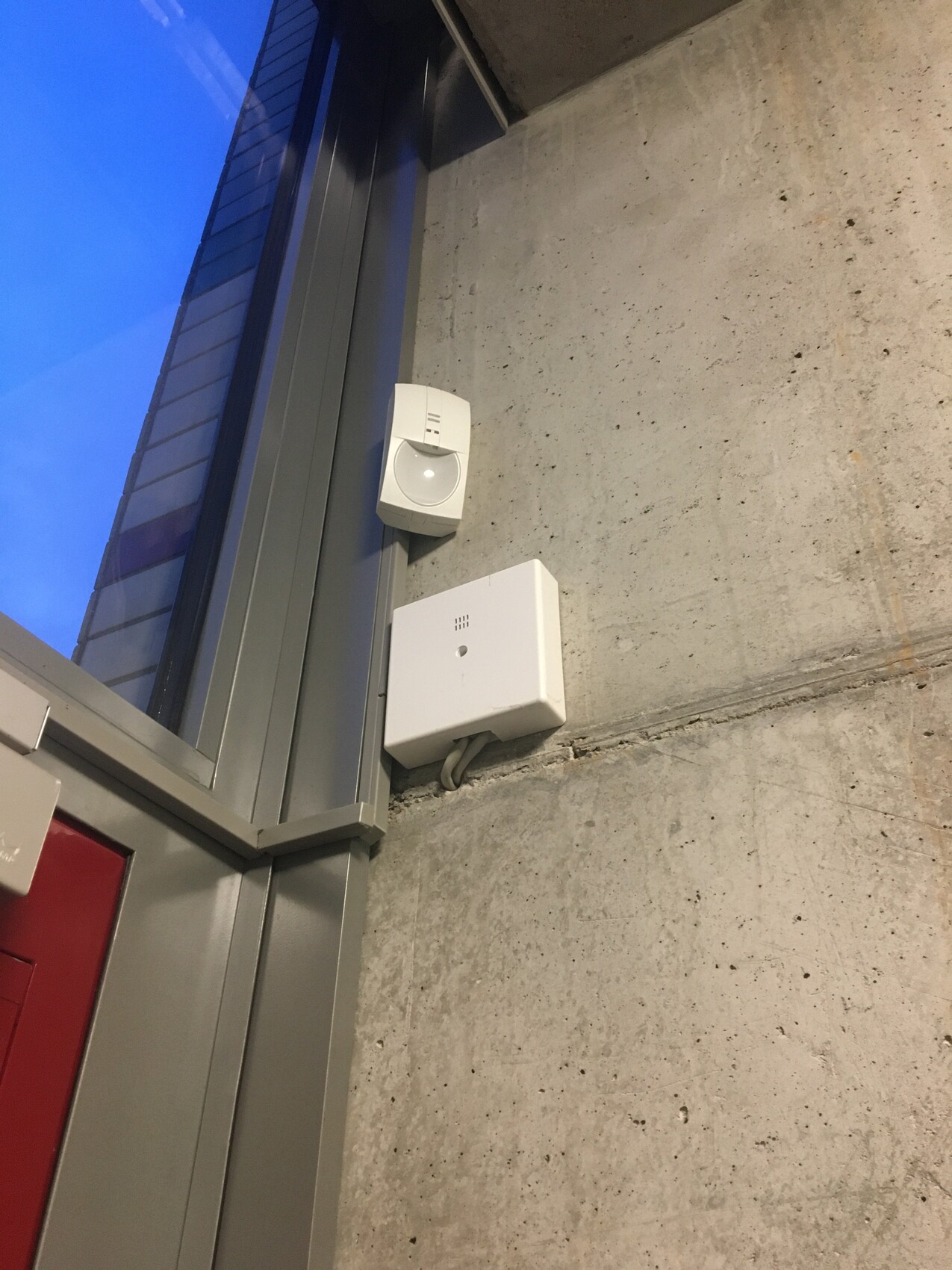 Wandmontierte Sicherheitssensoren und Alarmbox an roher Betonwand neben einem Fenster
