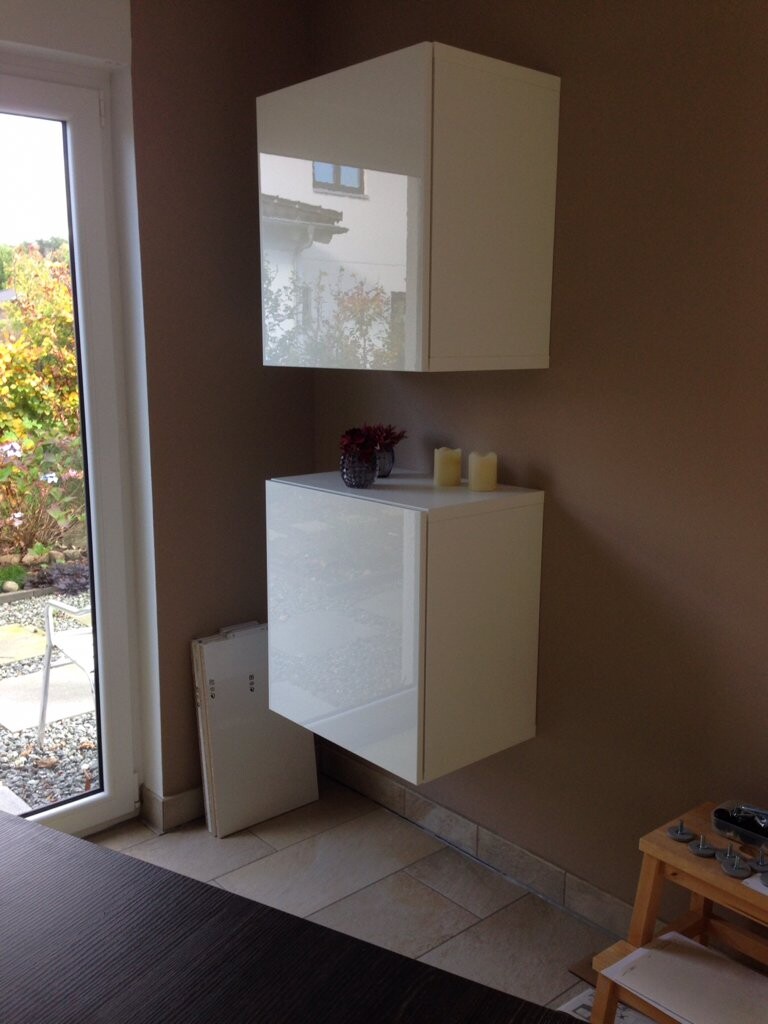 Moderne weiße Wandmöbel: Spiegelkasten über dem Schrank; Vase mit roten Blüten und zwei gelbe Kerzen.