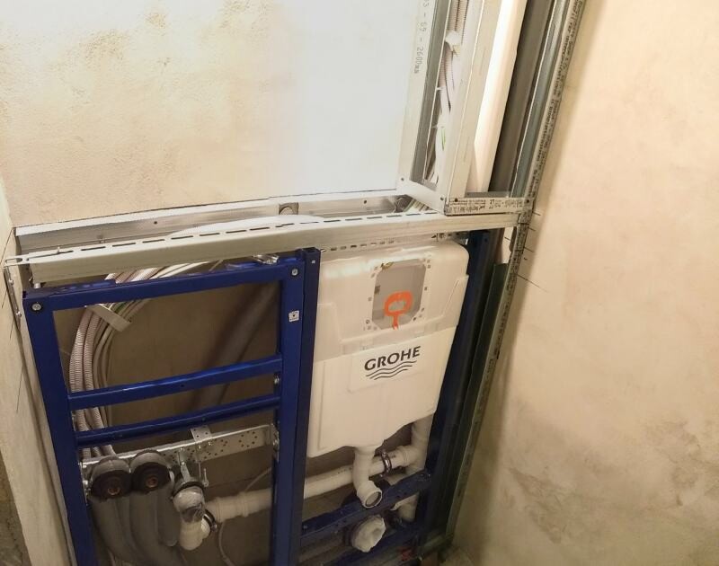 Blick in eine WC-Spülkasten-Installation: Metallrahmen, Grohe-Spülkasten, Rohrleitungen.