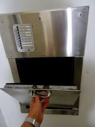 Wandmontierte Metallbox mit Einwurfklappe; eine Hand greift hinein