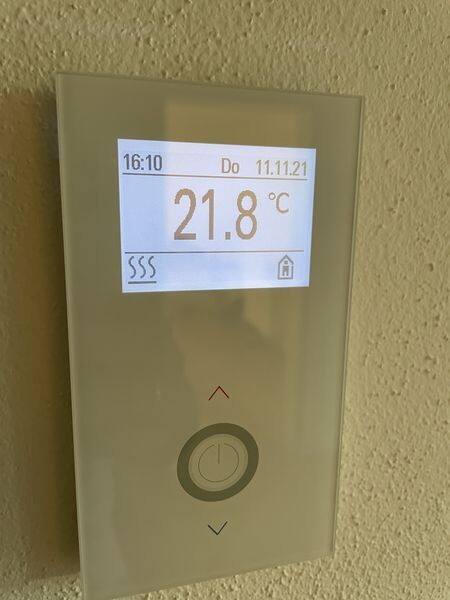Wandthermostat mit Display zeigt 21.8°C, Uhrzeit und Datum, runder Knopf.