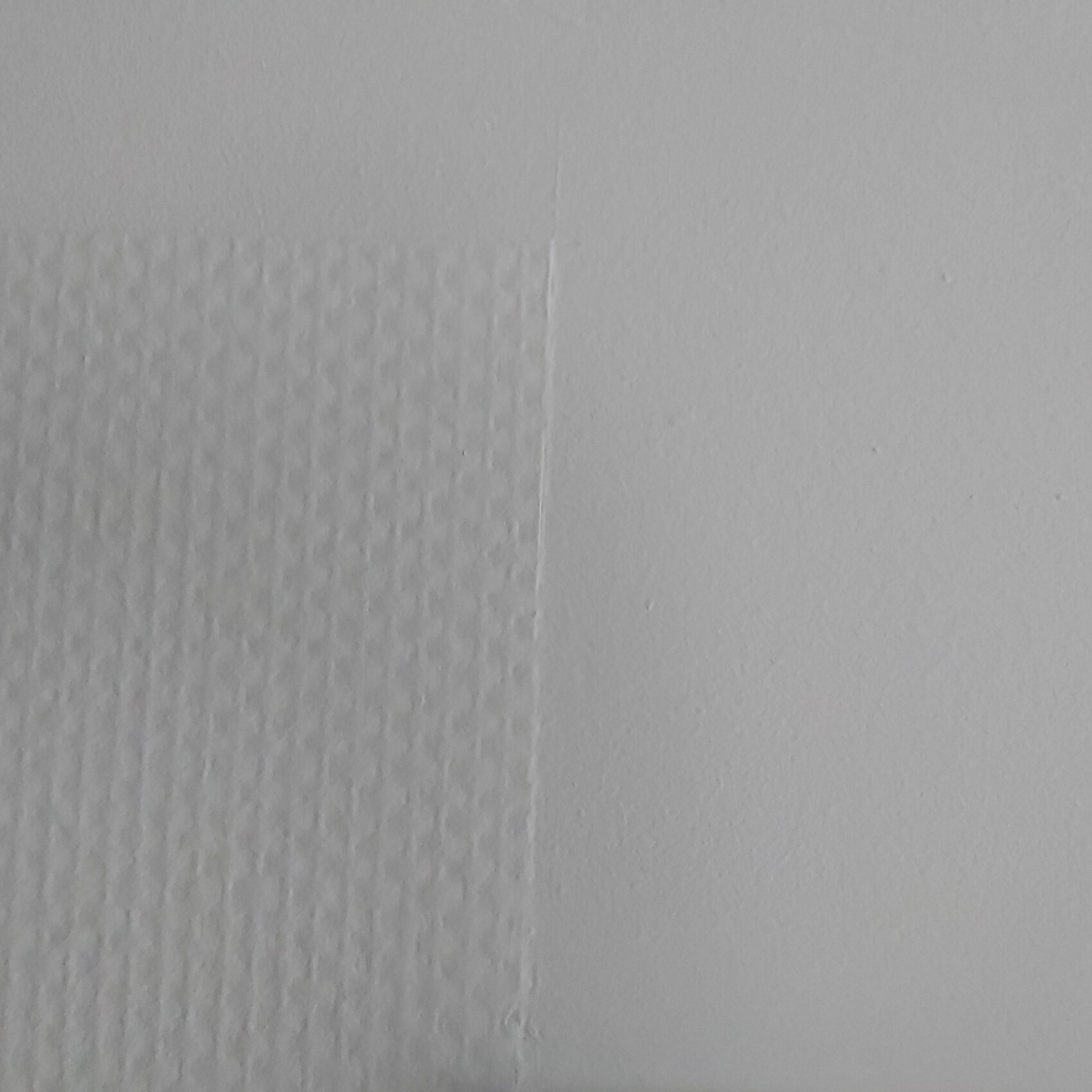 Nahaufnahme einer Wand mit zwei Oberflaechen: links Putz, rechts glatte Wand.