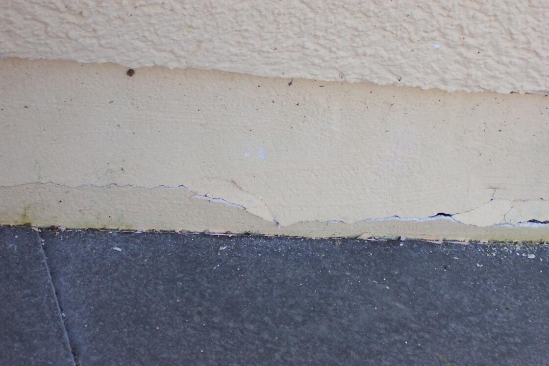 Außenwand mit Rissen und beschädigtem Putz am Bodenbereich