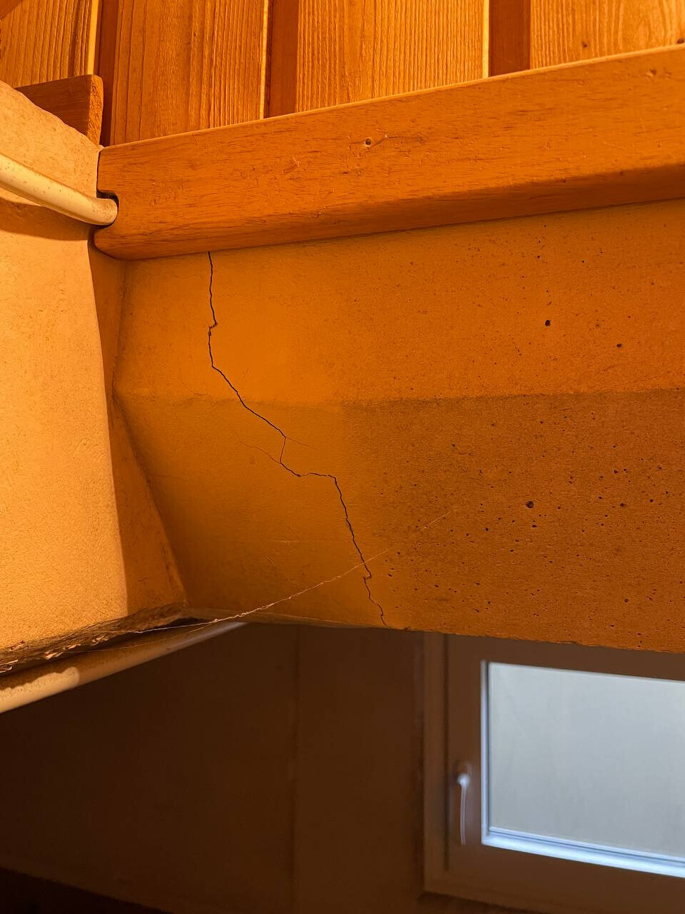 Innenraum: Holzverkleidung, Riss in gelber Wand unter Balken, Fenster unten rechts.