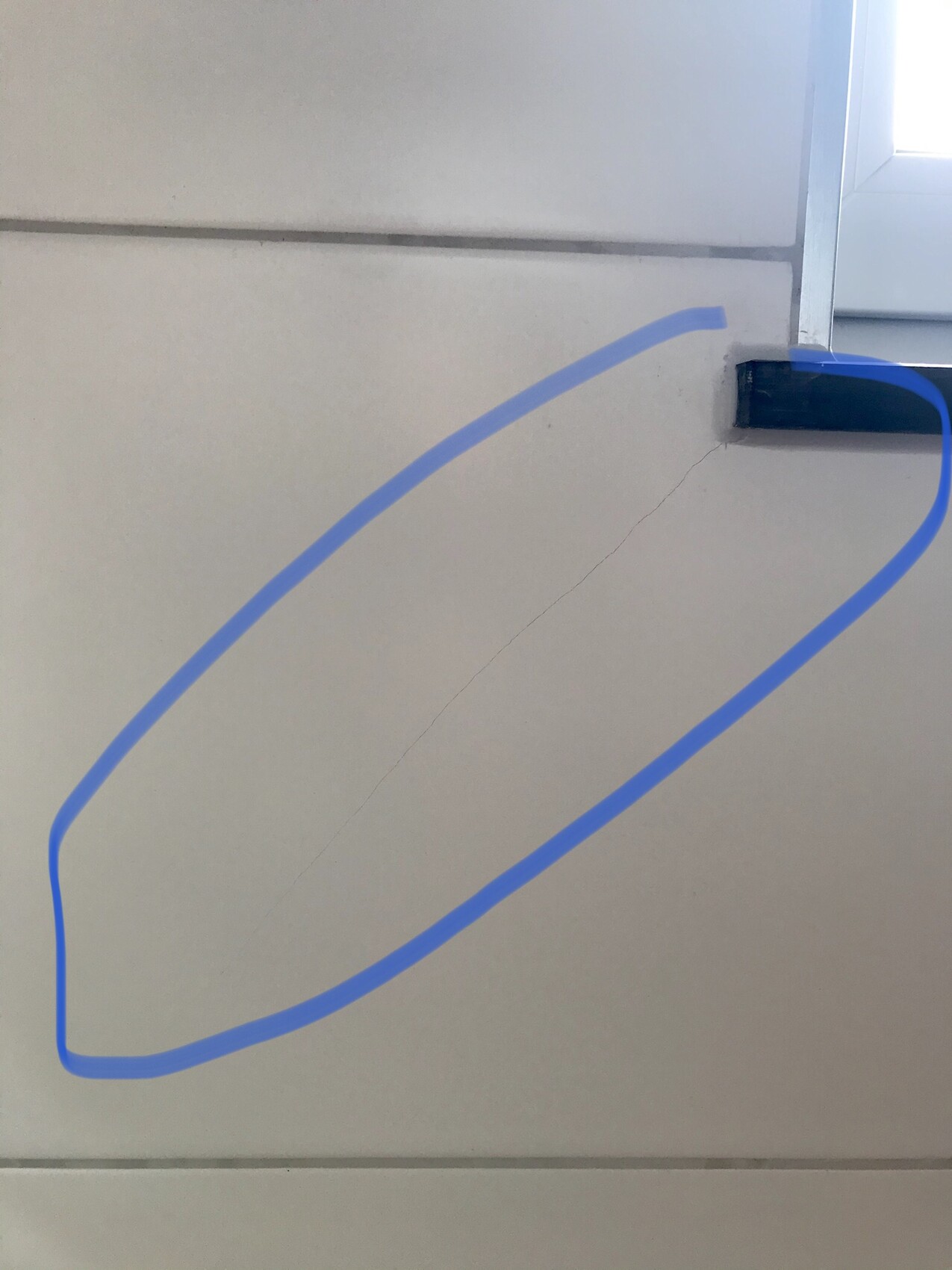 Blaue ovale Kontur auf grauer Wand; rechts Fensterrahmen sichtbar.