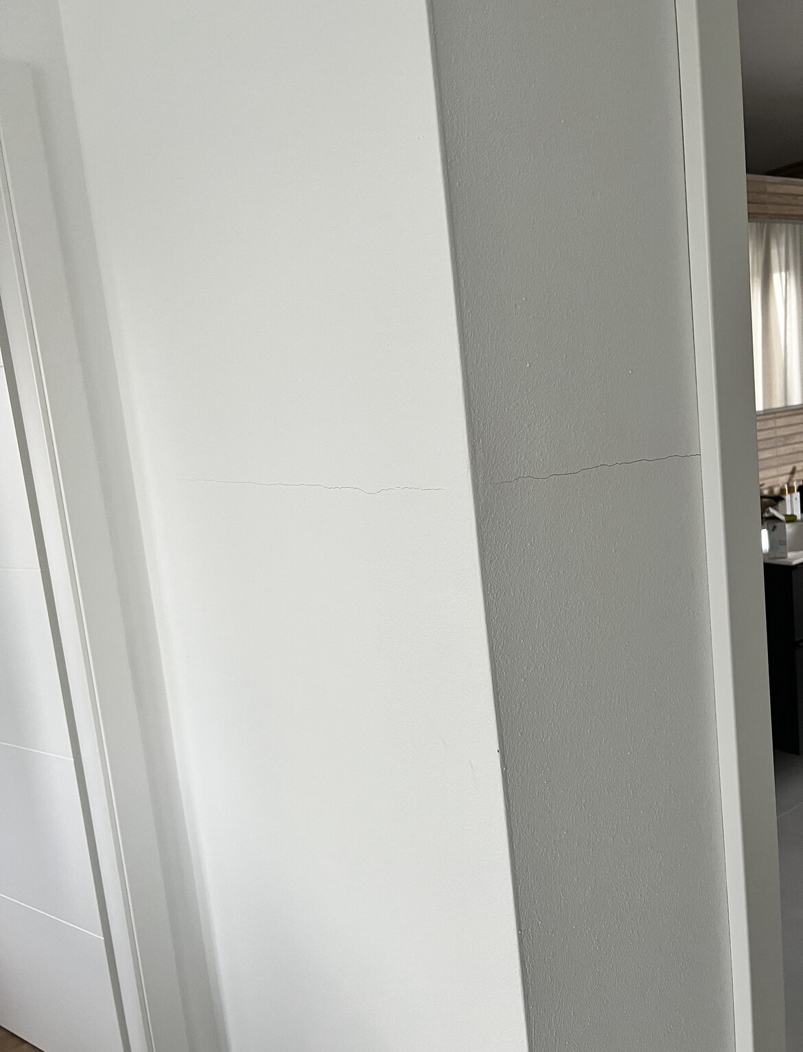 Innenraum: Weiße Wand mit feinem Haarriss, Türrahmen links und graue Wandseite rechts.