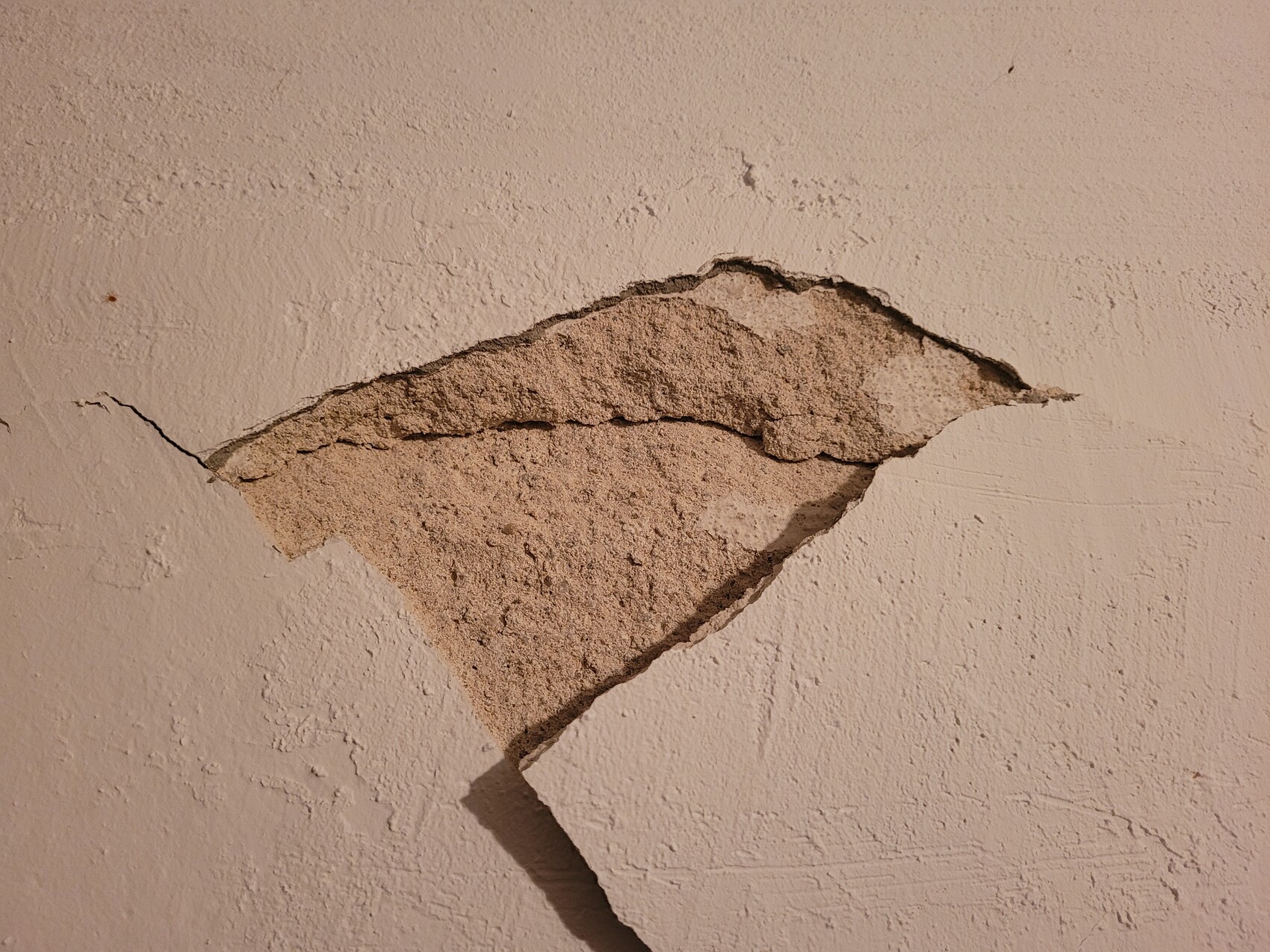 Verputzte Wand mit großem Loch; freigelegter, rauer Beton sichtbar.