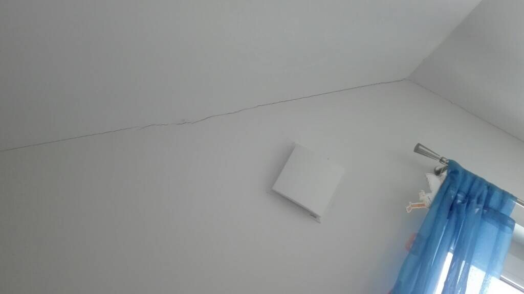 Ecke eines Zimmers mit Wandriss und blauem Vorhang.