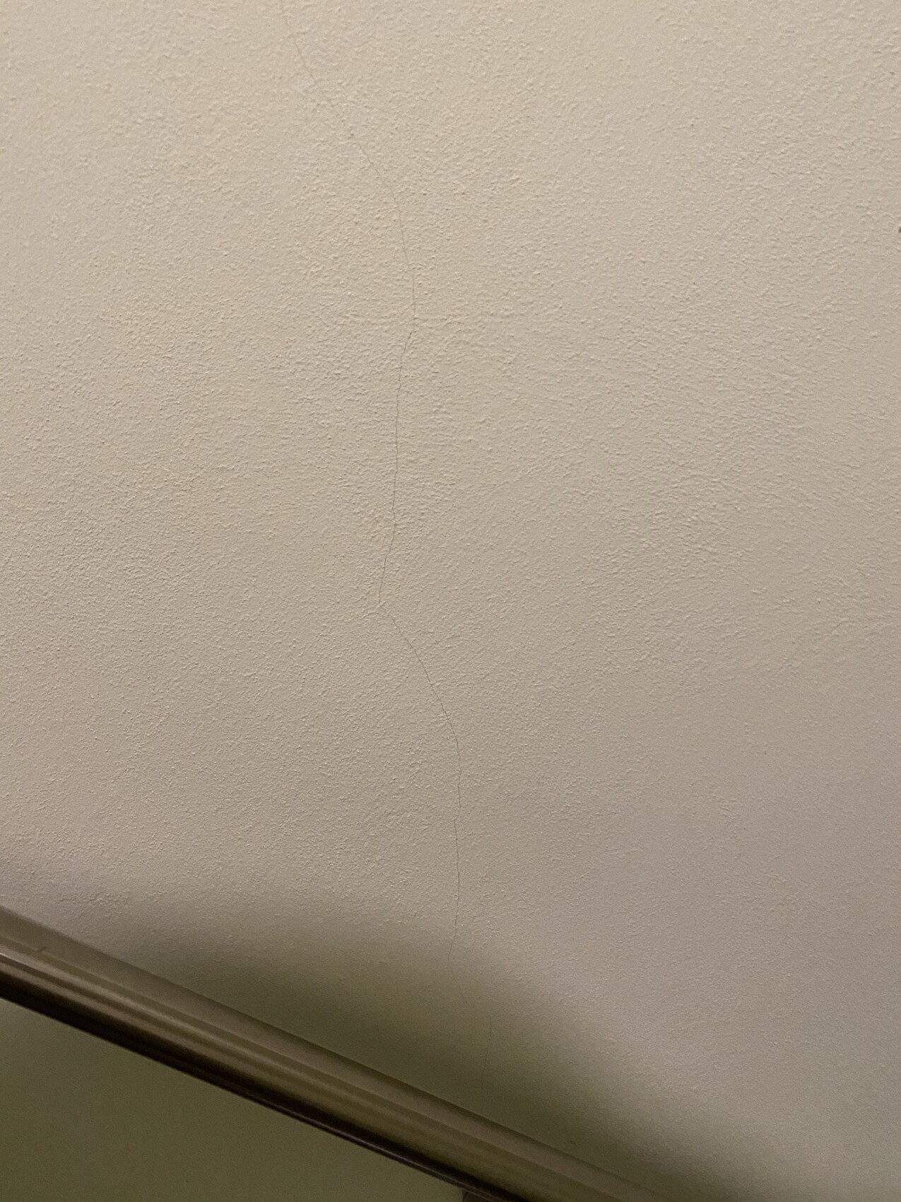 Nahaufnahme einer beigen Deckenoberfläche mit sichtbarem Riss, unten Zierleiste.