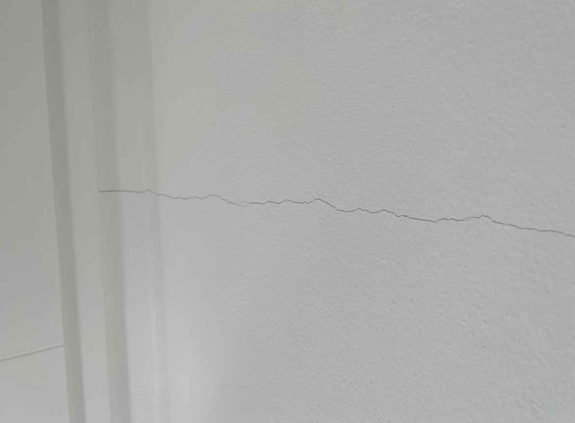 Weiße Wand mit einer horizontalen Risslinie von links nach rechts, neben Türrahmen.