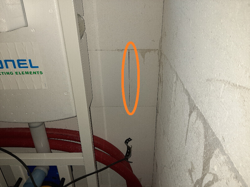 Eckbereich eines Technikraums: roter Schlauch, graues Gerätegehäuse, orange Fuge