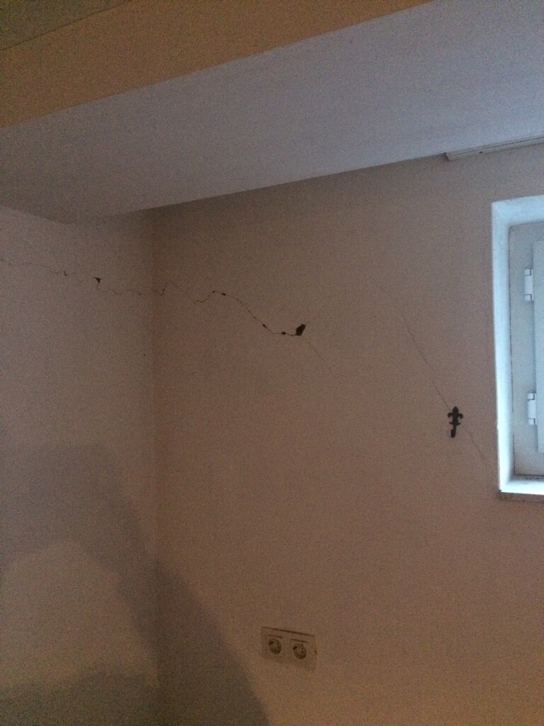 Innenraum mit Wandrissen, kleinem Fensterbereich und sichtbarer Steckdose.