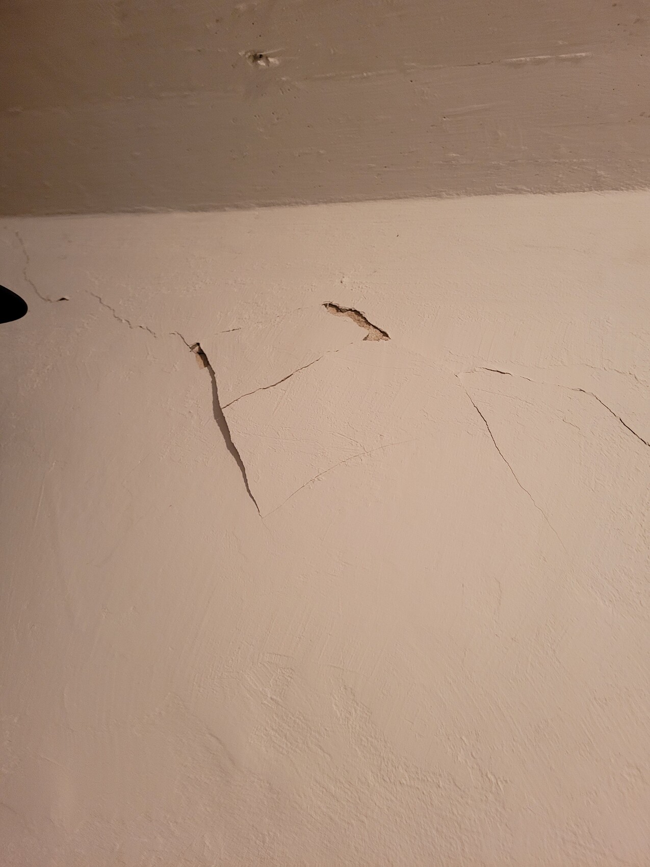 Beige Wand mit mehreren feinen Rissen und bröckelndem Putz.
