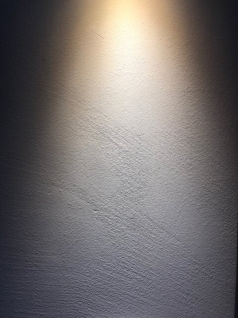 Rauhe Wand mit zentralem Lichtspot, heller Bereich in der Mitte und dunkle Ränder.