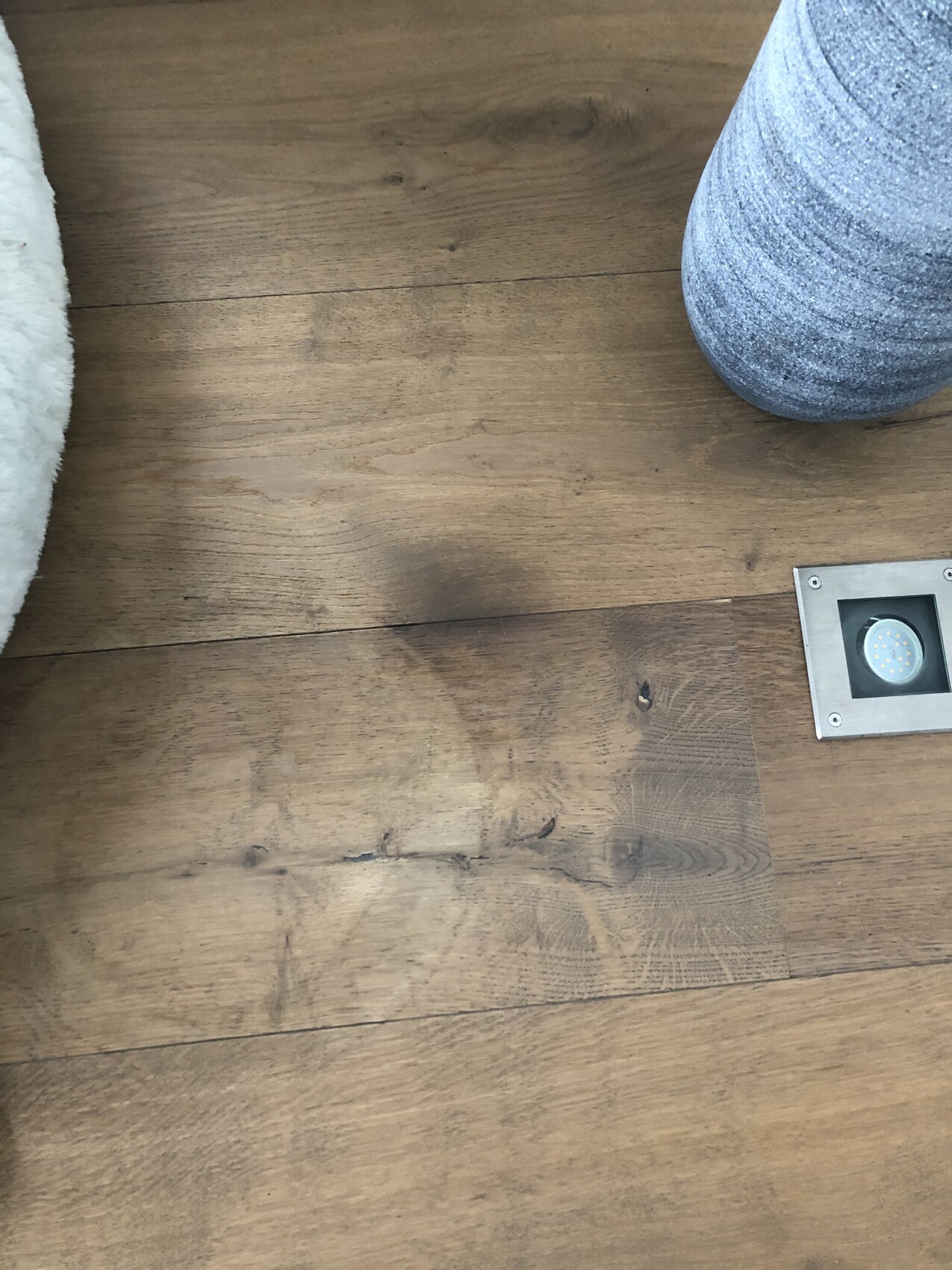 Holzboden mit LED-Leuchte grauer runder Sitzkissen und weiße flauschige Decke am Rand.