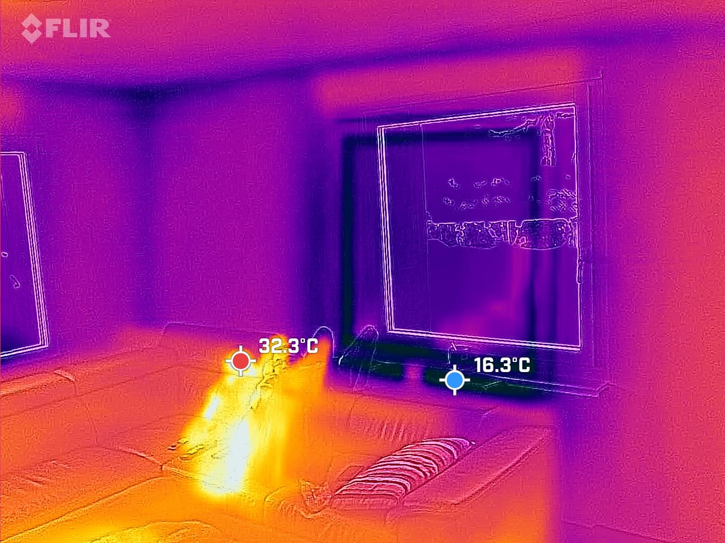 Thermische Aufnahme eines Wohnzimmers: Feuer brennt auf der Couch, links; Fenster rechts.