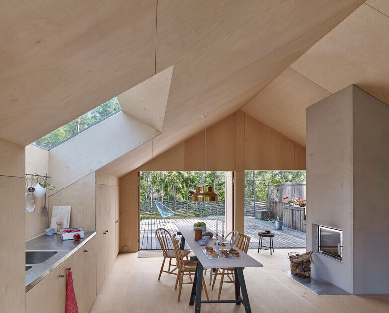 Heller Innenraum aus Holz mit Esstisch, Stühlen, Kamin und Terrassentür zum Garten.