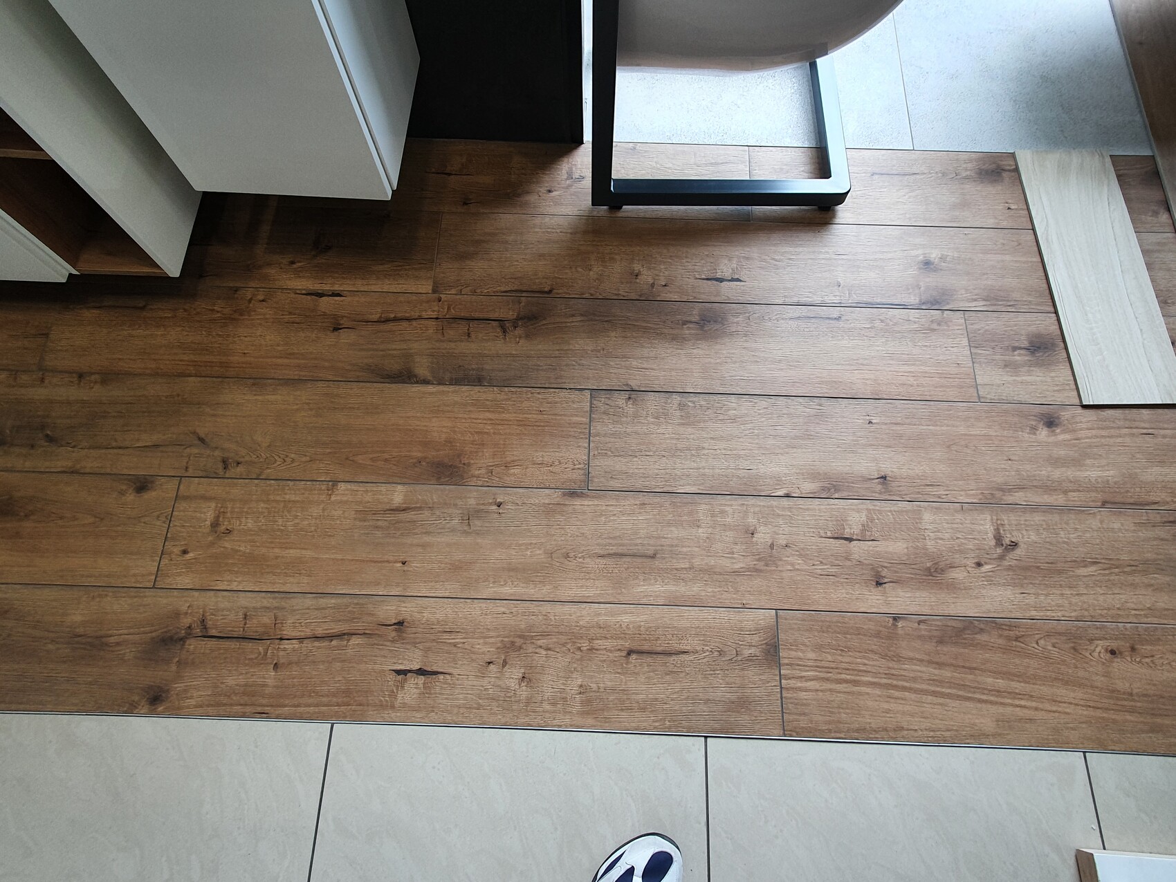 Brauner Holzboden mit Holzplanken, Metallrahmen eines Möbelstücks, Schuh unten im Bild.
