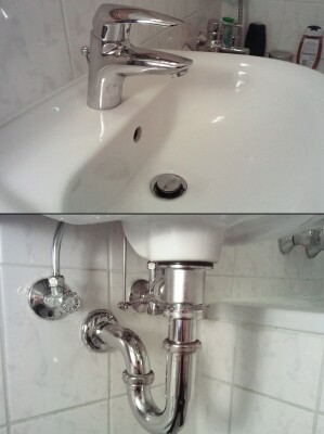 Waschbecken mit Armatur und sichtbaren Rohren unter dem Becken im Badezimmer.