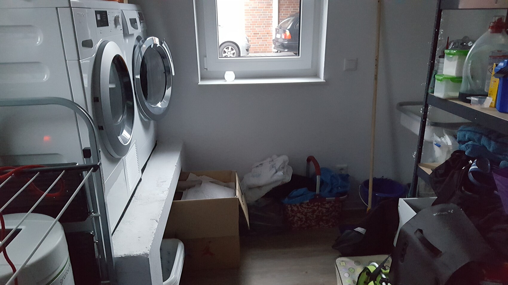 Waschraum mit zwei Frontlader-Waschmaschinen, Regalen und Lagerbehältern vor Fenster