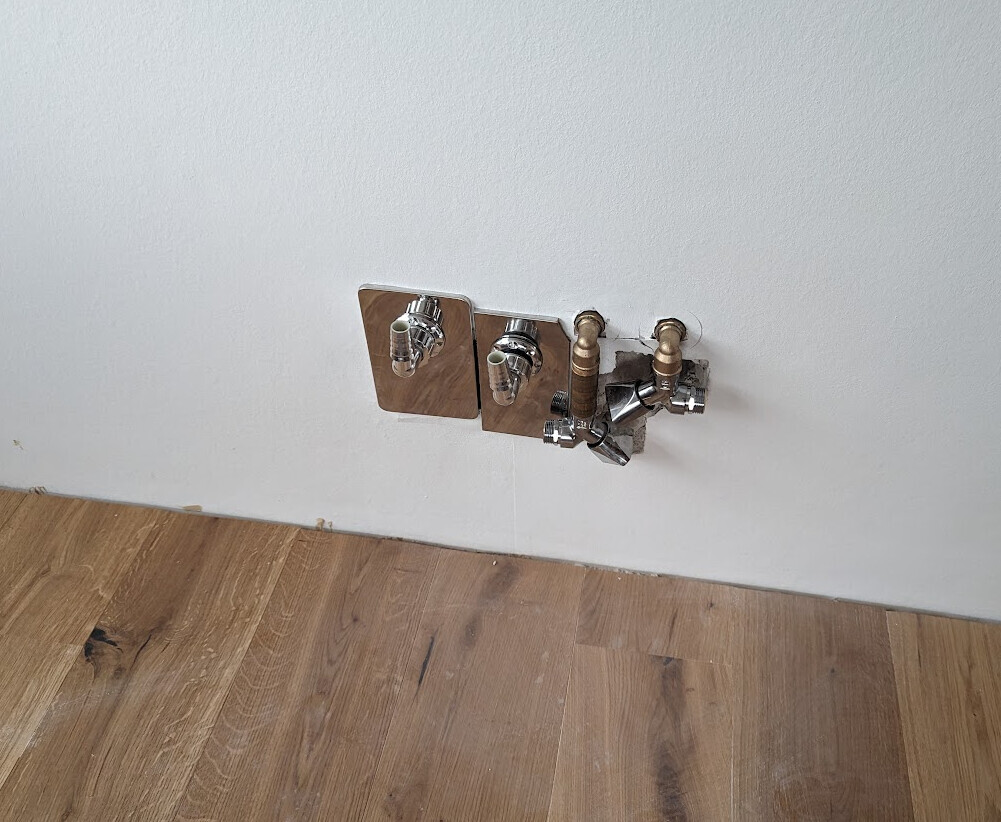 Wand mit Wasseranschlüssen: zwei Holzplatten mit Chromventilen und Kupferrohren.
