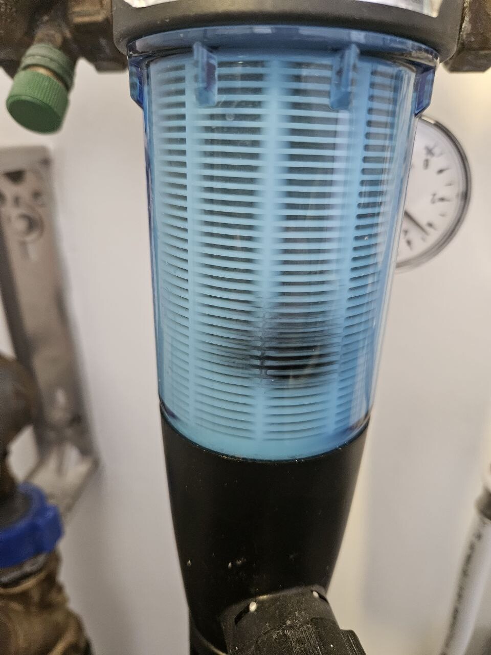 Blaue Filterpatrone in einem Hauswasserfiltersystem mit Messuhr im Hintergrund.