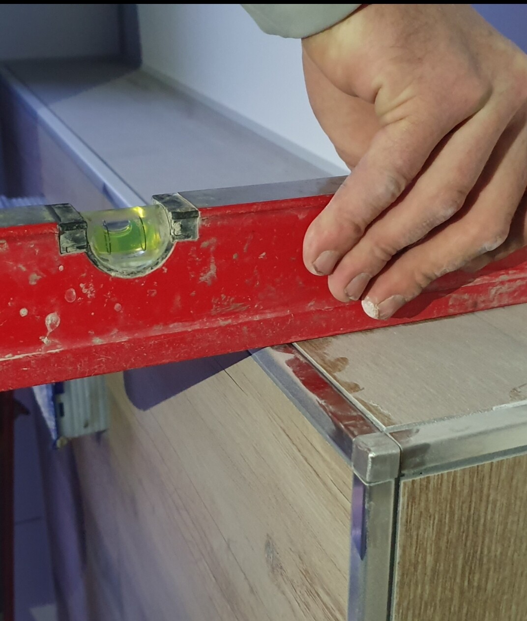 Nahaufnahme: Hand mit roter Wasserwaage prüft Waagerechte an einer Holzplatte.