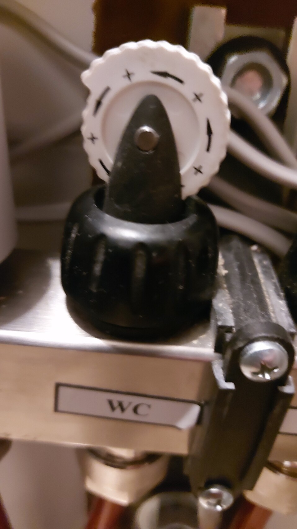 Nahaufnahme eines WC-Spülventils mit weißer Einstellkappe und schwarzem Griff.