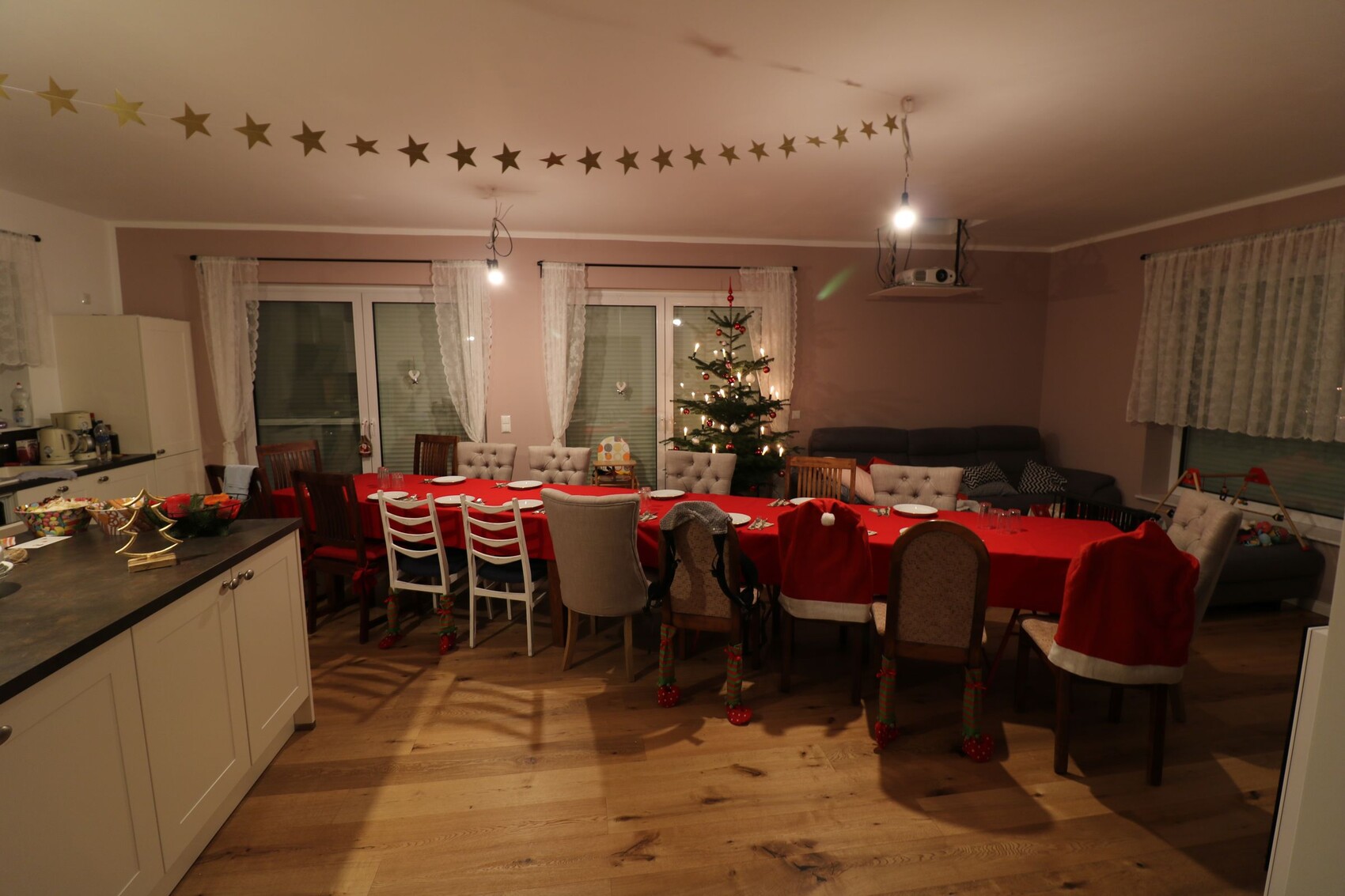Großes Esszimmer mit rotem Tisch, Weihnachtsbaum und Sternengirlande; Küche links.