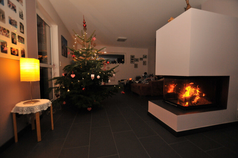 Gemütliches Wohnzimmer mit geschmücktem Weihnachtsbaum und brennendem Kamin.