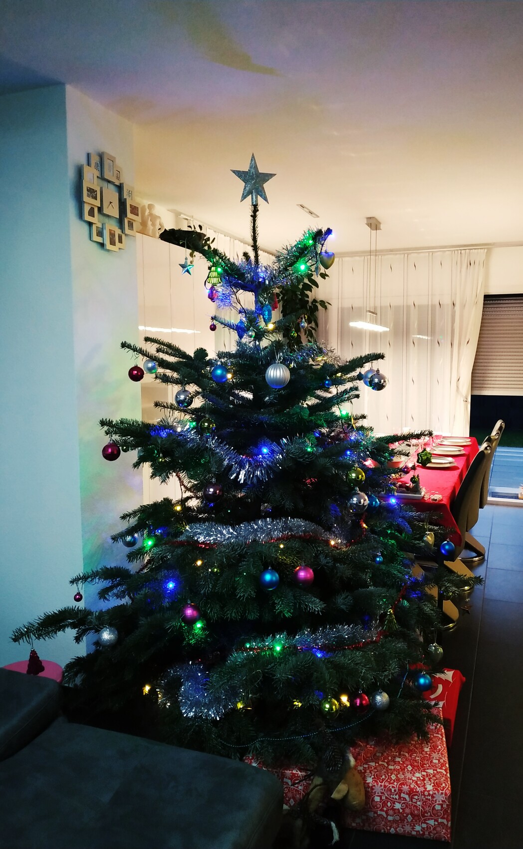 Weihnachtsbaum mit Stern, bunten Kugeln, Lichterketten und Geschenken im Wohnzimmer.