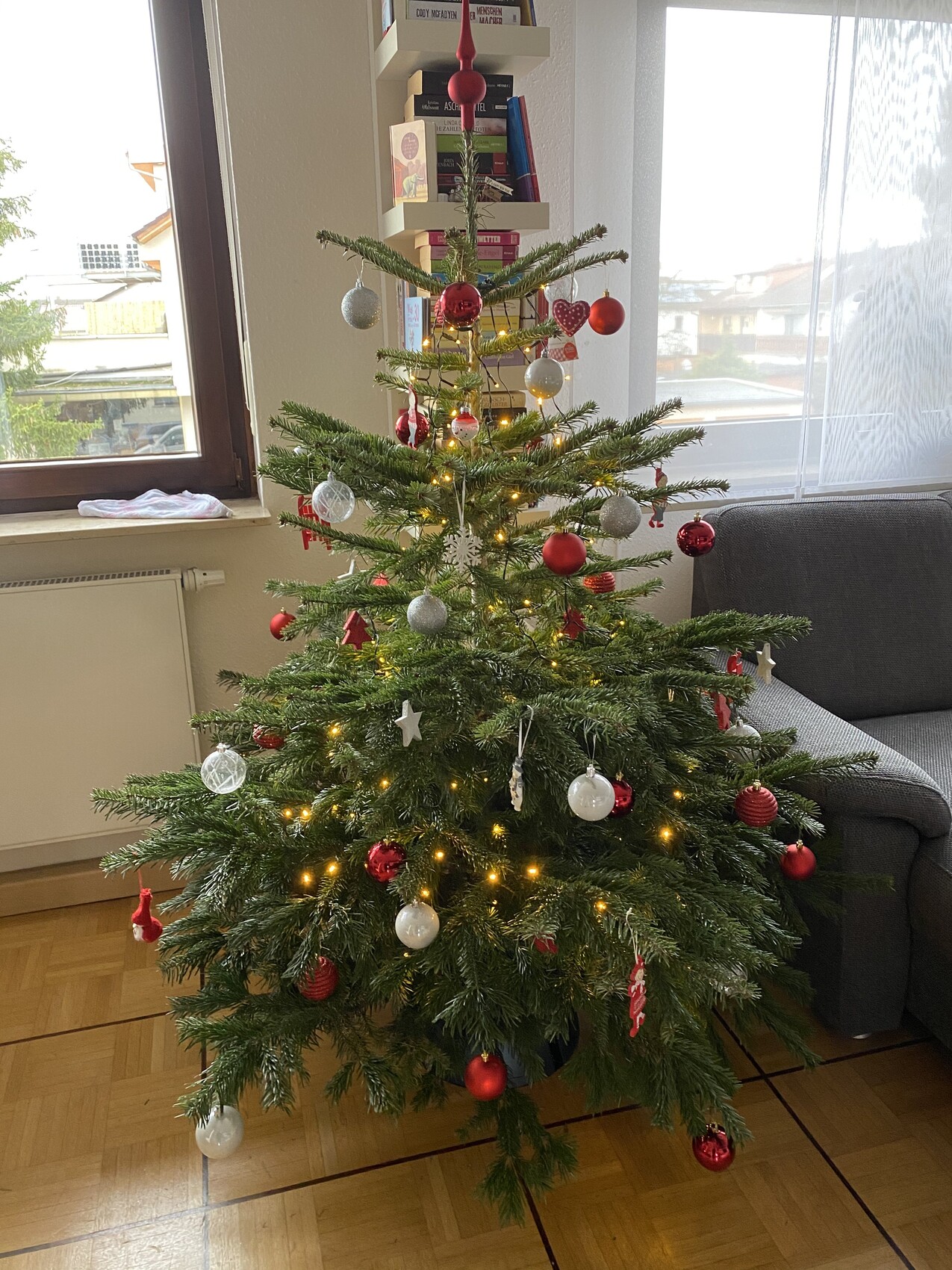 Weihnachtsbaum im Wohnzimmer, verziert mit roten und silbernen Kugeln und Lichterkette.