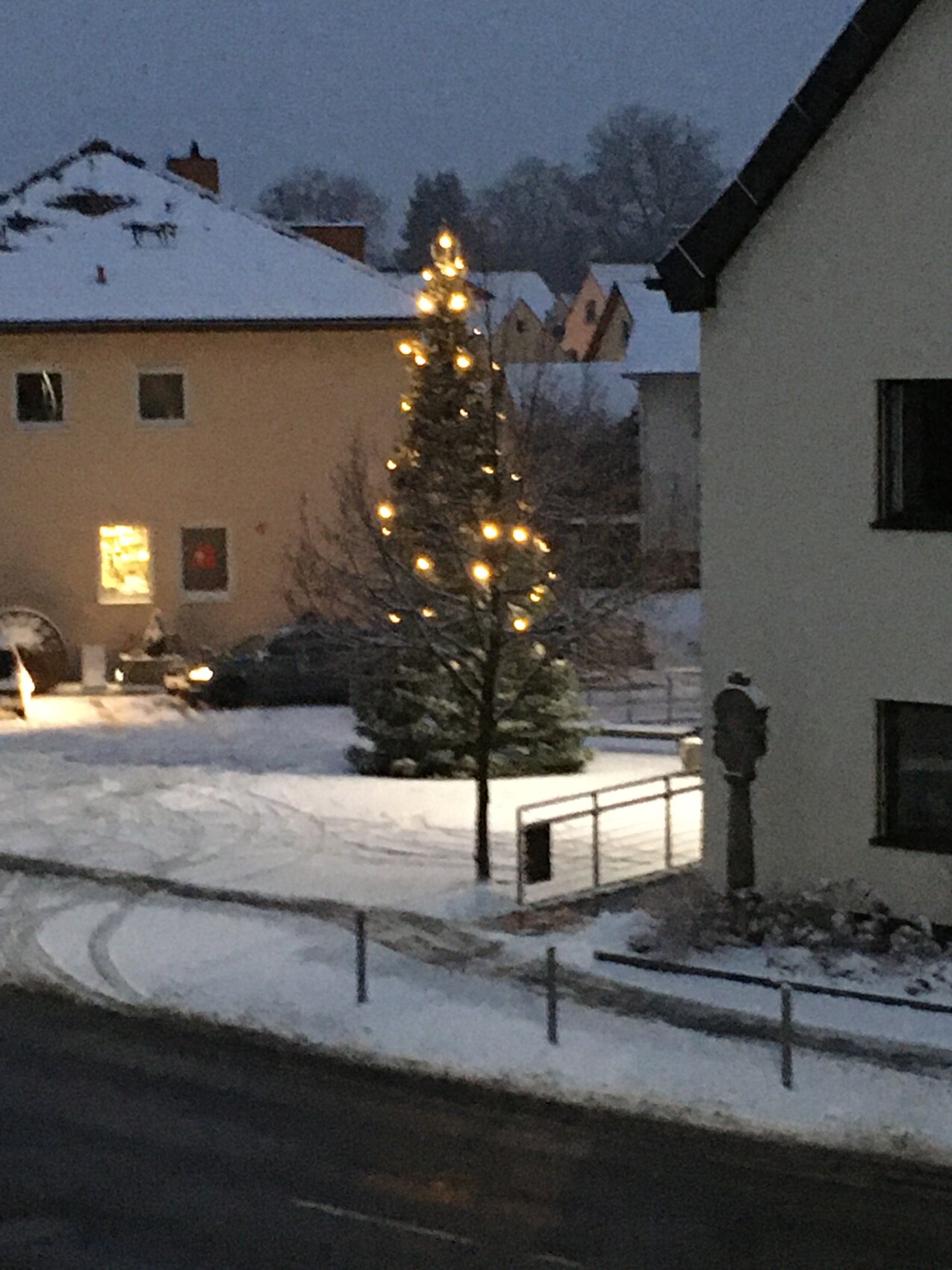 Außerhalb eines Wohngebiets steht ein beleuchteter Weihnachtsbaum im Schnee bei Dämmerung