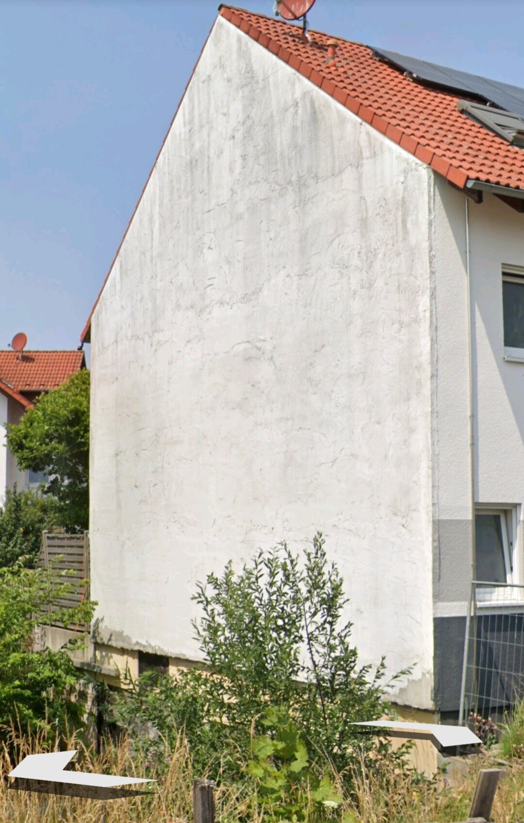 Außenansicht eines Hauses mit weiß verputztem Giebel, rotem Ziegeldach, Solarmodulen und Garten.