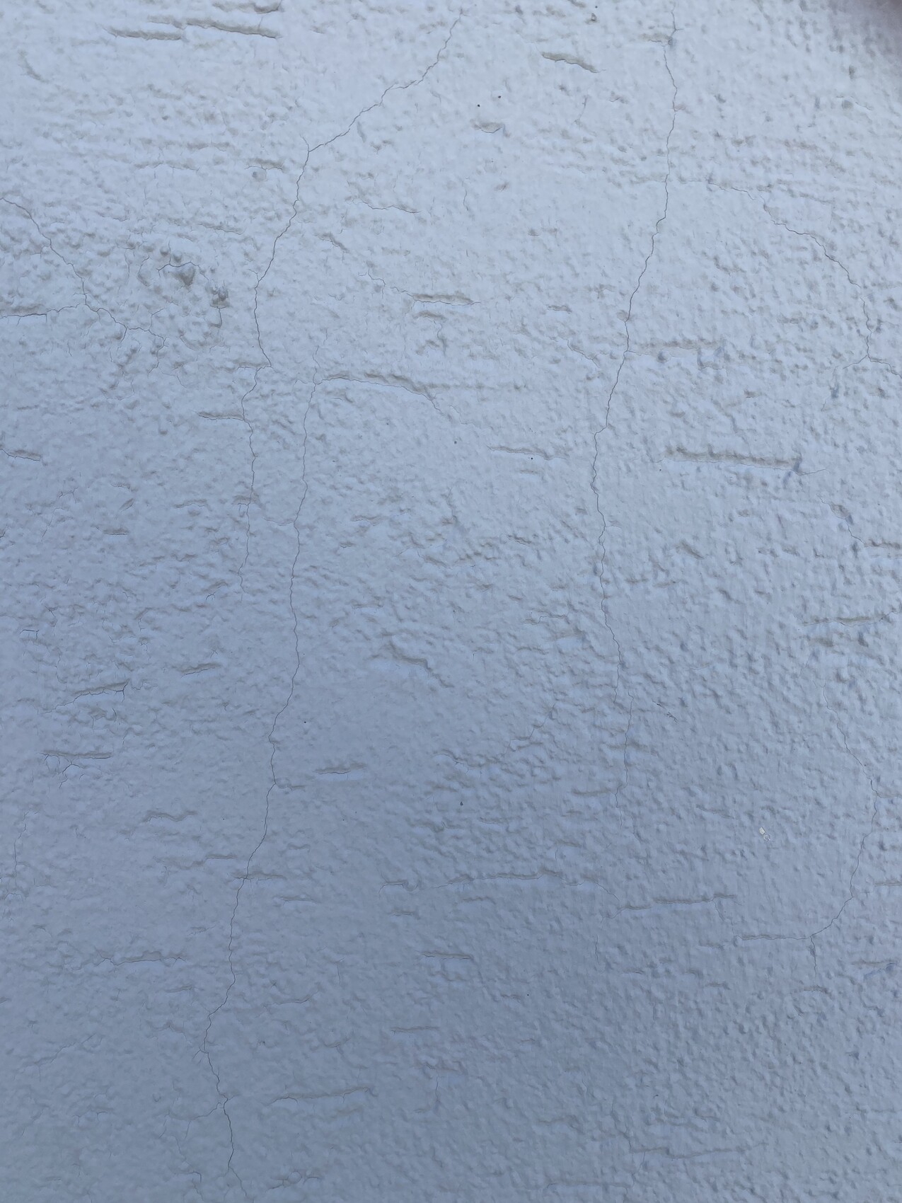 Bläulich getönte, grob texturierte Wand mit feinen Rissen und Unebenheiten