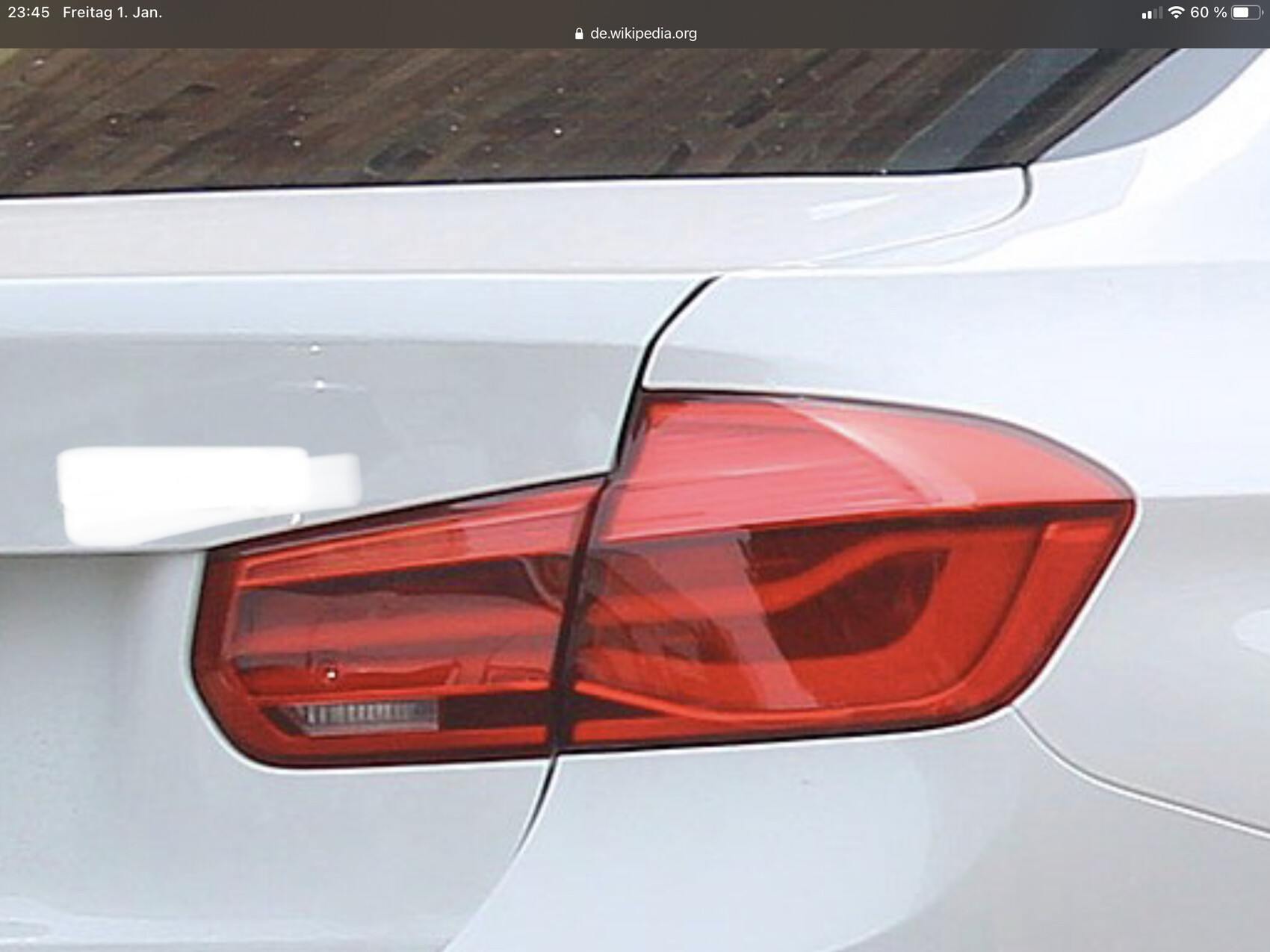 Rückseite eines weißen Autos mit roter Heckleuchte, seitliche Karosserie sichtbar.