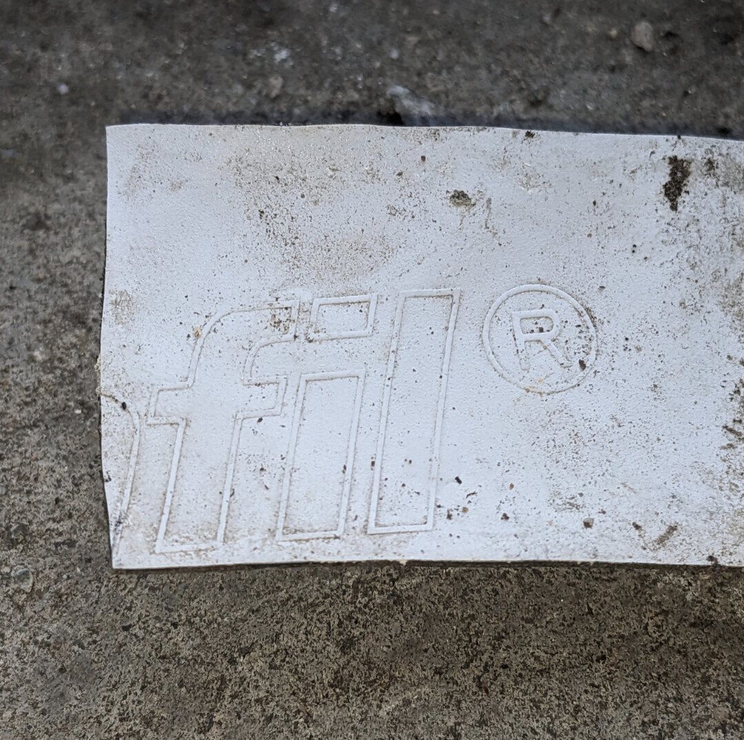 Staubiges weißes Etikett mit geprägtem Logo und ®-Symbol auf grobem Betonboden.